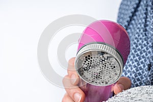 Woman is removing lint with fabric shaver or fuzz remover