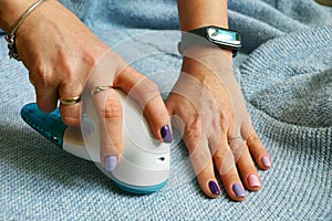 The woman is removing the lint from the sweater. Wireless device for cleaning knitted fabrics from lint