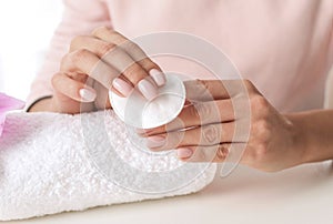 Woman removing polish from nails with cotton pad at table