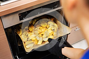 Woman removing prepared potatoes tray out of oven