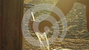 Woman removing sand form her legs under beach shower near sandy ground, morning sun shines in background, detail on water drops
