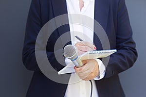 Woman reporter or journalist at media event, holding microphone, writing notes. Broadcast journalism concept.