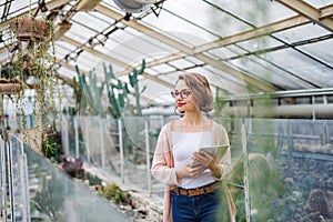 Woman researcher standing in greenhouse, using tablet.