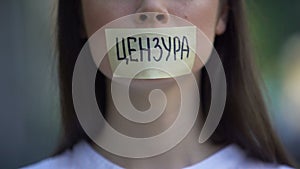 Woman resolutely taking off tape with censored word in russian over mouth