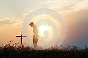 Woman respecting at the cross on the field of sunset background