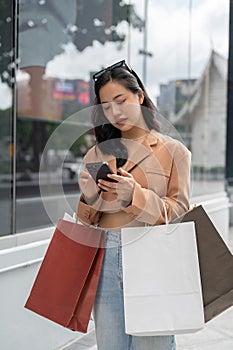 A woman responding to messages on her smartphone while walking in the city with her shopping bags