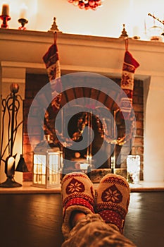 Woman is rest by the fireplace in red slippers on Holidays. Closeup photo of feet in woolen socks.