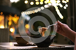 Woman in a restaurant on the terrace eating rice noodles. ramen in a plate, thai food