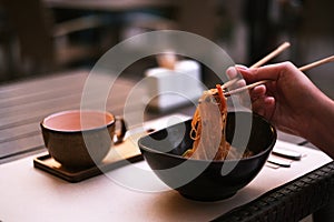 Woman in a restaurant on the terrace eats rice noodles with chopsticks. ramen in a plate, thai food