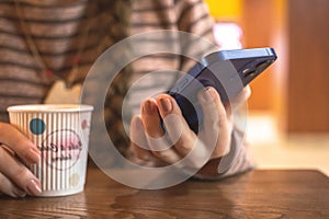 Woman in restaurant using modern mobile phone in hand with coffe cup on a wooden table. Communication concept photo