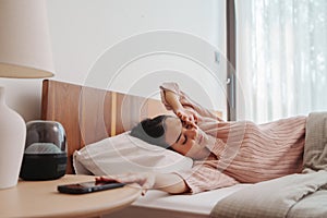 Woman resting in bed with a headache, sunlight from window, serene mood