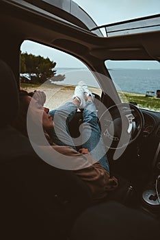 woman resting in car parked at sea beach