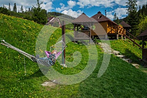 A woman resting in the hammock in the mountains. wooden houses on the background and the green grass