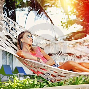 Woman is resting in the hammock under the palms on the tropical