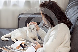 A woman resting at home, reading magazines and stroking her cat