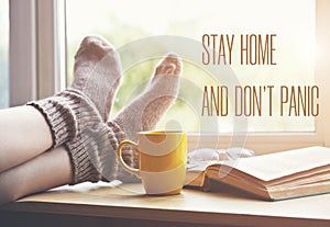 Woman resting keeping legs in socks on table with coffee and reading book