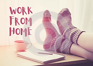 Woman resting keeping legs in warm socks on table with morning coffee and notebook