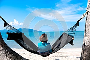 woman resting looking at the sea and mountains She sits in a hammock on a tropical beach. Beautiful tourism concept on the island