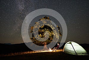 Woman resting at night camping in mountains under starry sky