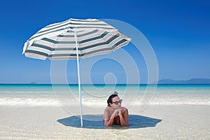 Woman resting under a beach umbrella.