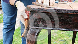 A woman restores old furniture in the fresh air. Vintage table. Wearing rubber gloves