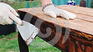 A woman restores old furniture in the fresh air. Vintage table. Wearing rubber gloves