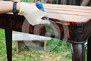 A woman restores old furniture in the fresh air. Vintage table. Wearing rubber gloves