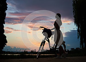 Woman with retro bike under the sky at sunset. Enjoying beautiful view of evening sky with clouds colorful in summer