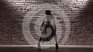 Woman rhythmic in high heels dance twerk against a brick wall. Slow motion