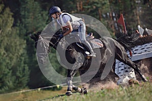 Woman rider and black sport horse galloping energetically during eventing competition