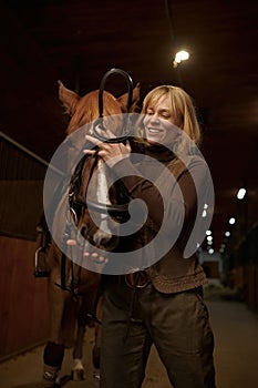 Woman rider harnessing horse in stable of riding club or ranch