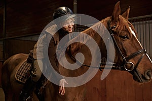 Woman rider in saddle praises bay horse affectionately patting neck