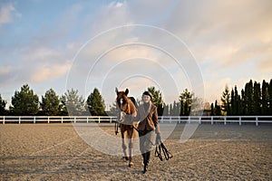 Woman rider walking horse side by side holding harness saddle-girth