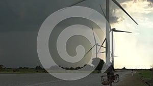 Woman rides bicycle along wide asphalt road by windmills