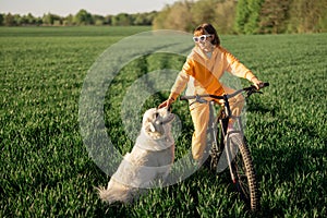 Woman rides a bicycle on a field with her dog