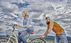 Woman rides bicycle sky background. Push and promoting. Impulse to move. Man pushes girl ride bike. Support helps