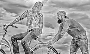 Woman rides bicycle sky background. Service and assistance. Man helps keep balance ride bike. Girl cycling while man