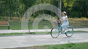 Woman rides bike in park at sunset. Happy smiling girl in hat and dress is cycling on vintage old bicycle in sunset light. Carefre