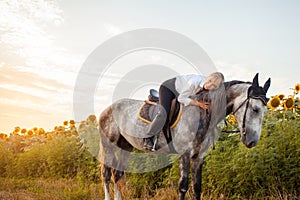 woman rides a gray horse in a field at sunset. Freedom, beautiful background, friendship and love for the animal. Sports