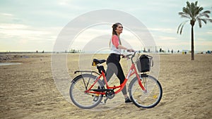 Woman riding bicycle along beach sand at summer time