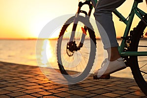 Woman riding bicycle on embankment at sunset