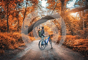 Woman riding a bicycle in forest in autumn at sunset