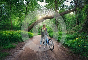 Woman riding a bicycle in forest in spring at sunset