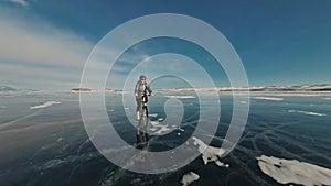 Woman is riding bicycle on the ice. The girl is dressed in a silvery down jacket, cycling backpack and helmet. Ice of