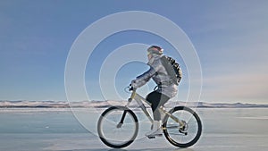 Woman is riding bicycle on the ice. The girl is dressed in a silvery down jacket, cycling backpack and helmet. Ice of