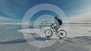 Woman is riding bicycle on the ice. The girl is dressed in a silvery down jacket, cycling backpack and helmet. Ice of