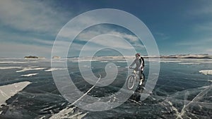 Woman is riding bicycle on the ice. The girl is dressed in a silvery down jacket, cycling backpack and helmet. Ice of