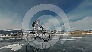 Woman is riding bicycle on the ice. The girl is dressed in a silvery down jacket, cycling backpack and helmet. Ice of