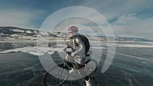 Woman is riding bicycle on the ice. The girl is dressed in a silvery down jacket, cycling backpack and helmet. Ice of