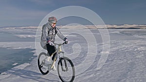 Woman is riding bicycle on the ice. The girl is dressed in a silvery down jacket, cycling backpack and helmet. Ice of